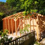 timber wooden frame of a wooden garage being built with trees in the background and a fence in the foreground